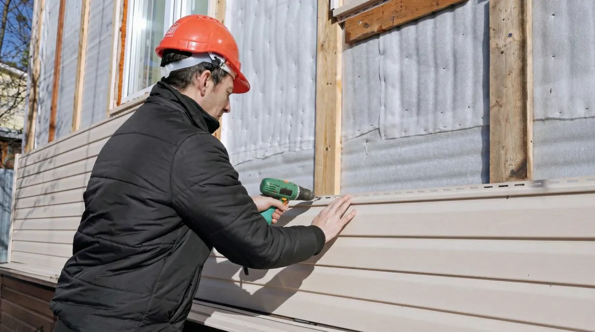 Siding replacement professional using a power drill to install new tan vinyl siding on a home exterior in Madison, WI